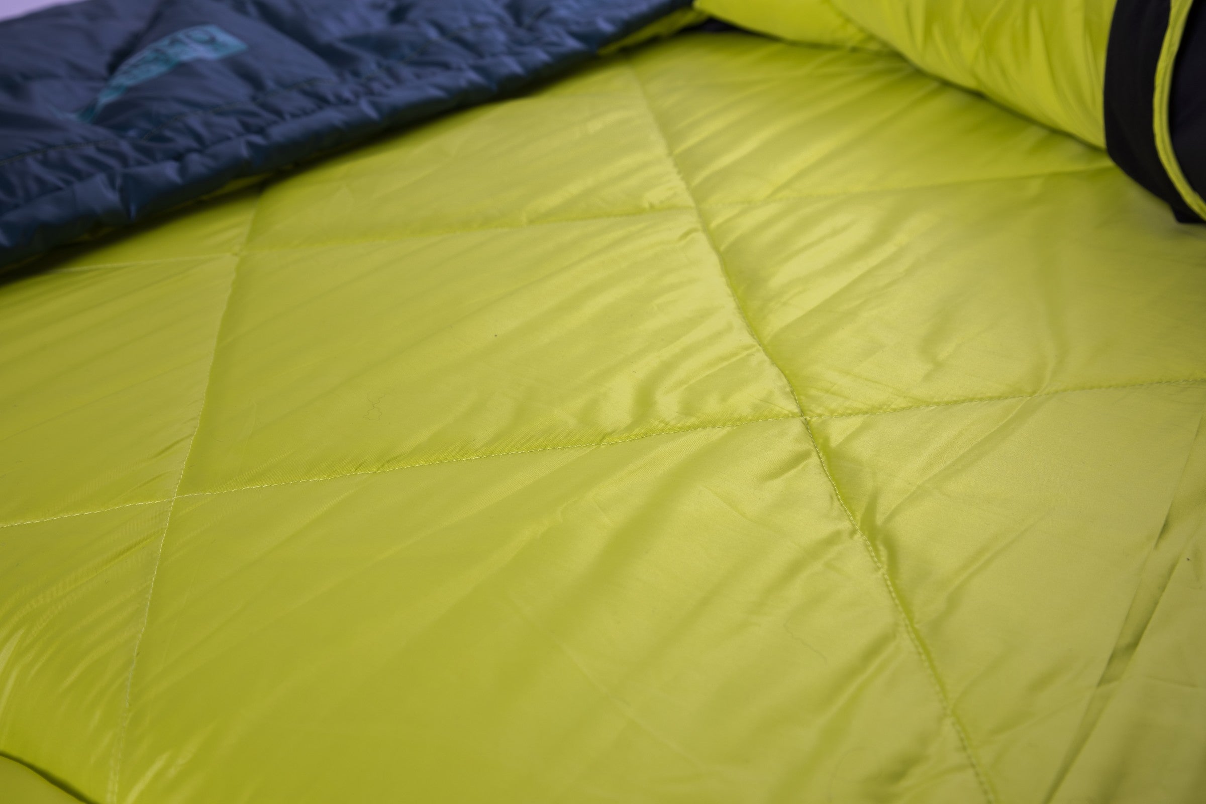Close-up of the NEMO Equipment Jazz™ Double Synthetic Sleeping Bag in lime green, showing visible stitching and a partially unzipped design that reveals its dark green interior.